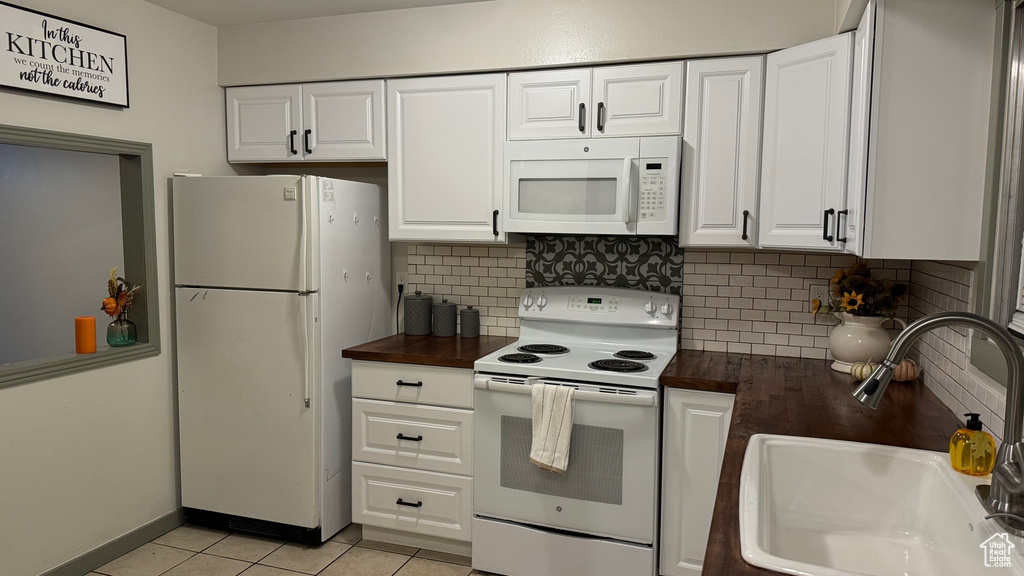 Kitchen featuring tasteful backsplash, white cabinetry, light tile patterned flooring, sink, and white appliances