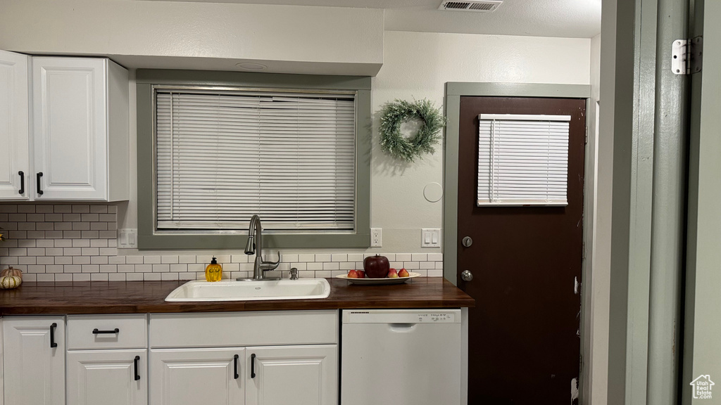 Kitchen with tasteful backsplash, sink, dishwasher, wood counters, and white cabinetry