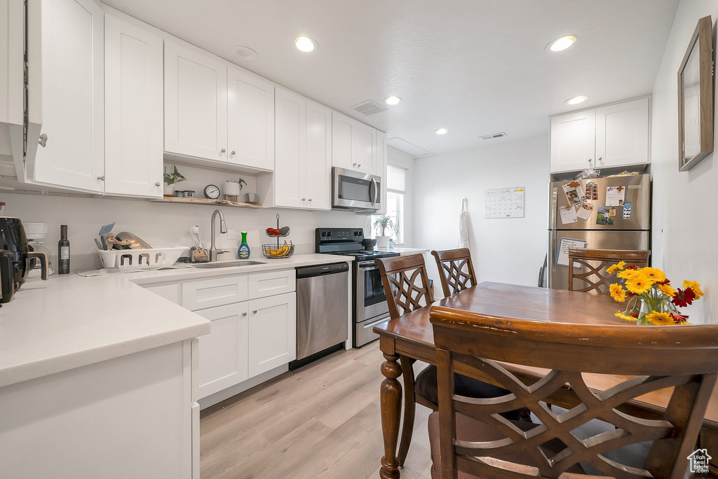 Kitchen with light hardwood / wood-style flooring, appliances with stainless steel finishes, sink, and white cabinets