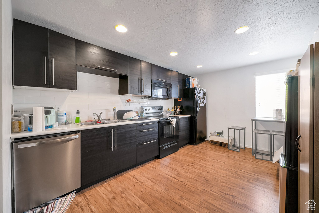 Kitchen featuring black appliances, sink, light wood-type flooring, a textured ceiling, and decorative backsplash