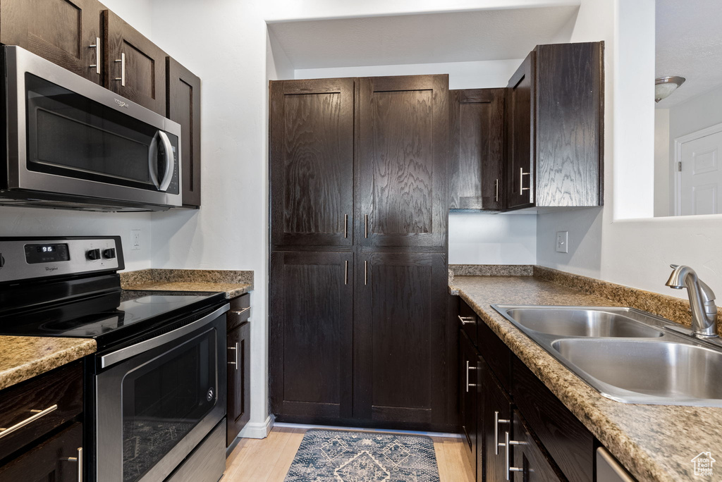 Kitchen featuring dark brown cabinetry, light hardwood / wood-style floors, appliances with stainless steel finishes, and sink