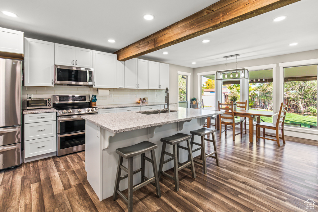 Kitchen featuring dark wood-type flooring, appliances with stainless steel finishes, a center island with sink, and white cabinets