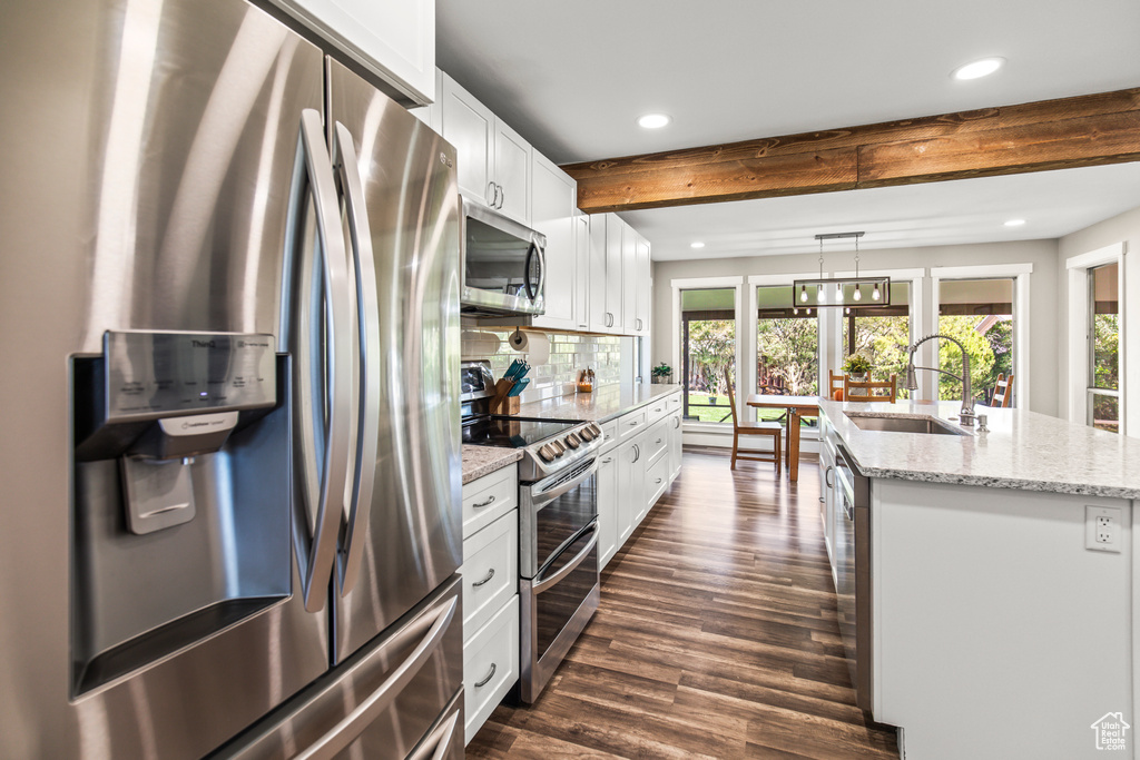 Kitchen featuring appliances with stainless steel finishes, sink, dark hardwood / wood-style flooring, white cabinetry, and a kitchen island with sink