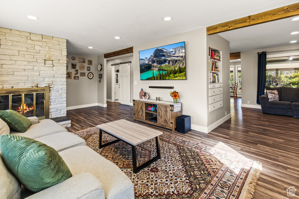 Living room featuring beam ceiling, dark wood-type flooring, a barn door, and a stone fireplace