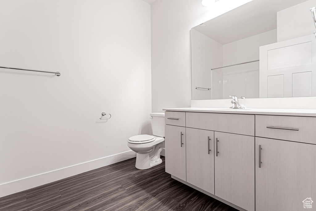 Full bath featuring toilet, vanity, baseboards, and wood finished floors