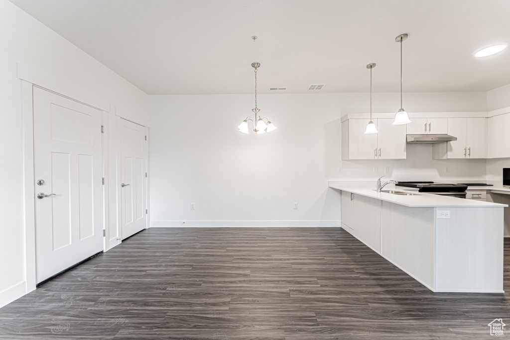 Kitchen featuring under cabinet range hood, a notable chandelier, white cabinetry, and light countertops