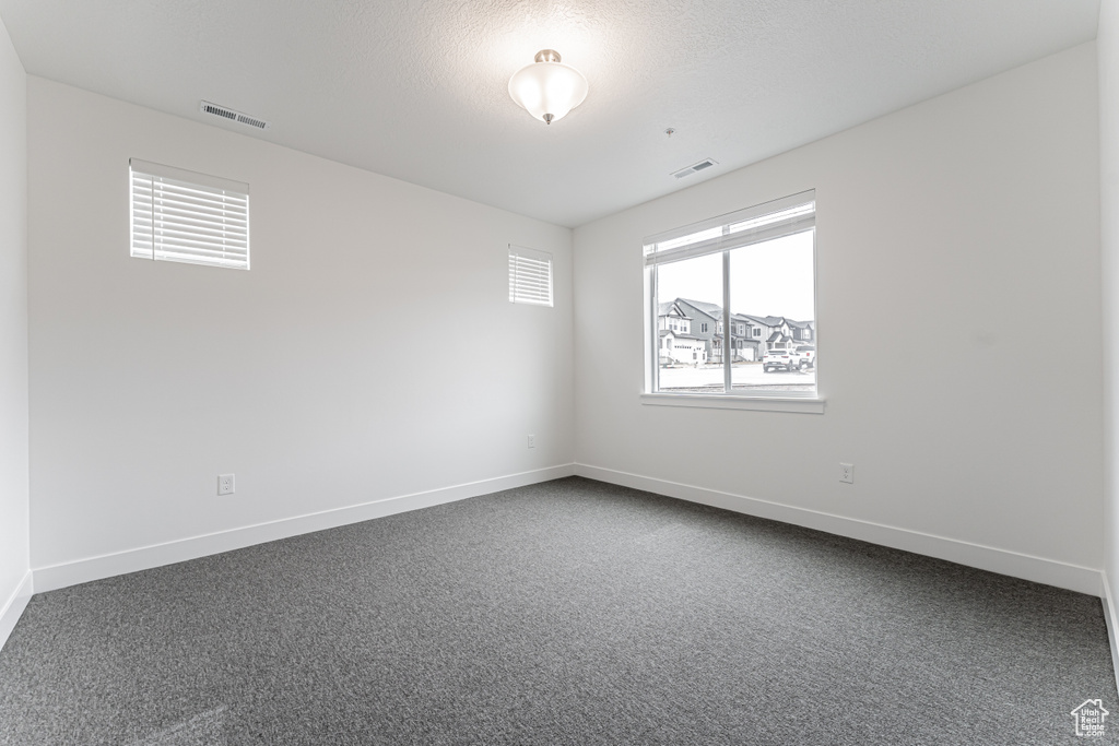 Unfurnished room with visible vents, dark carpet, and baseboards