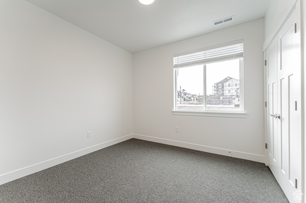 Unfurnished bedroom with visible vents, baseboards, and dark colored carpet