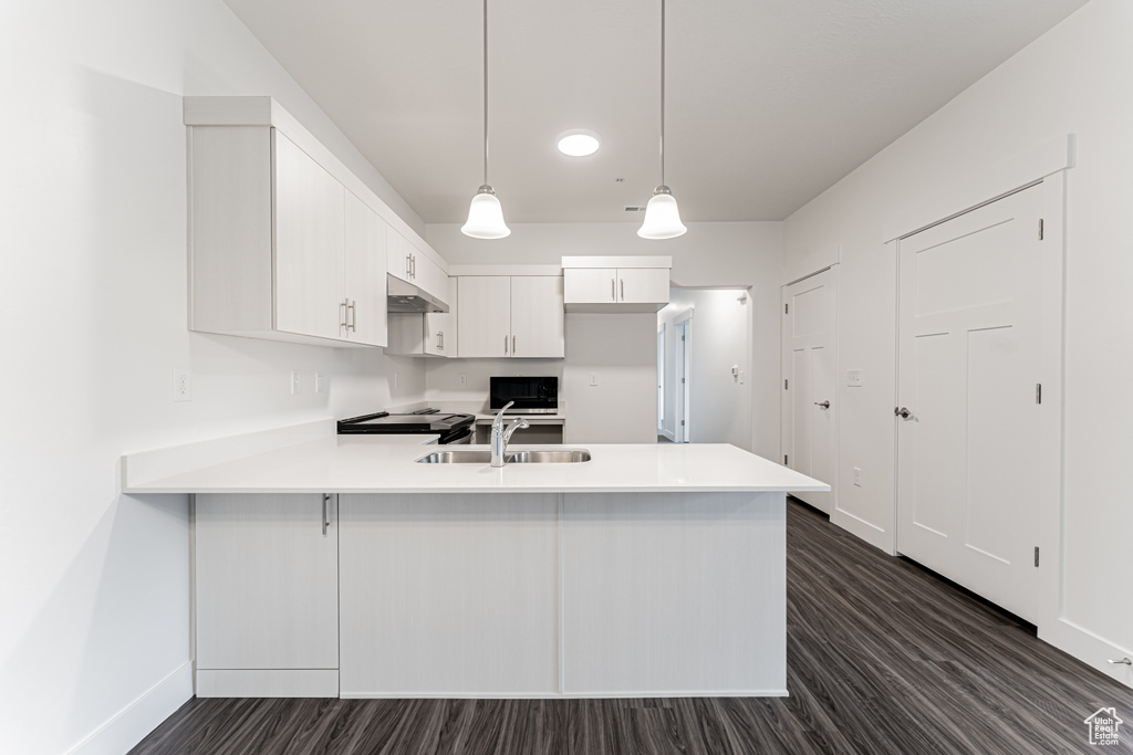 Kitchen featuring dark wood-type flooring, a sink, a peninsula, white cabinets, and light countertops