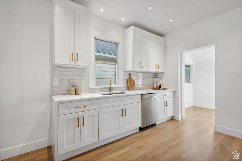 Kitchen with white cabinetry, stainless steel dishwasher, and backsplash