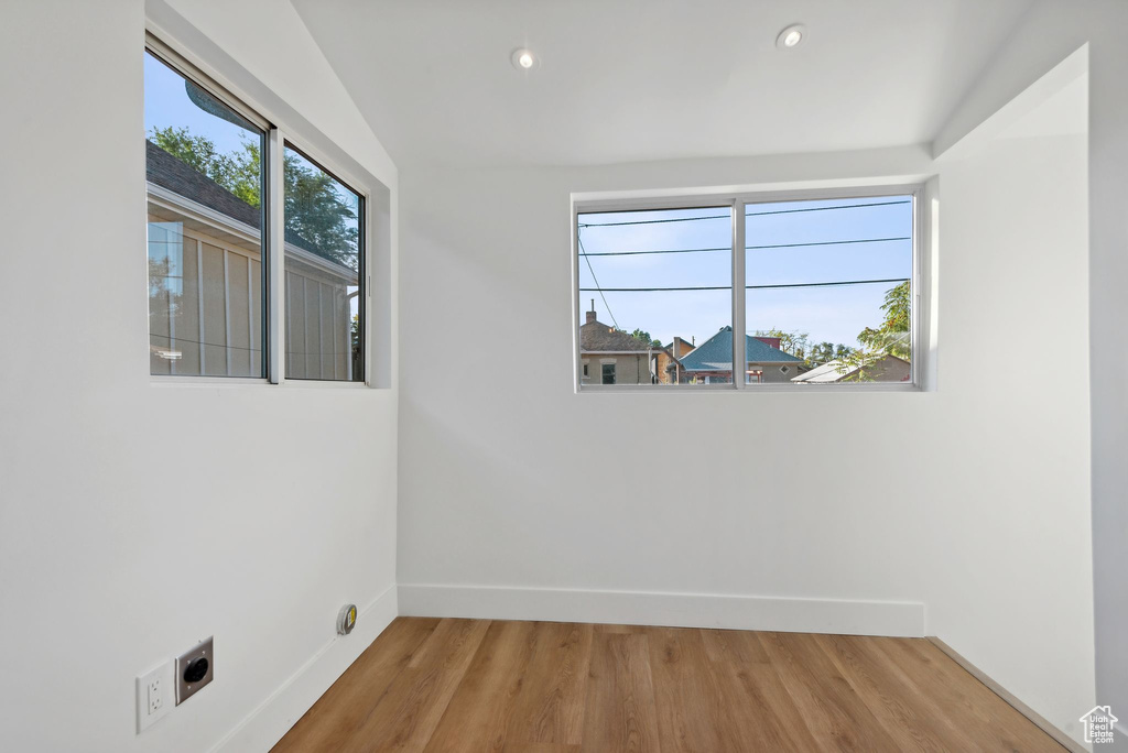 Empty room with hardwood / wood-style floors, vaulted ceiling, and plenty of natural light