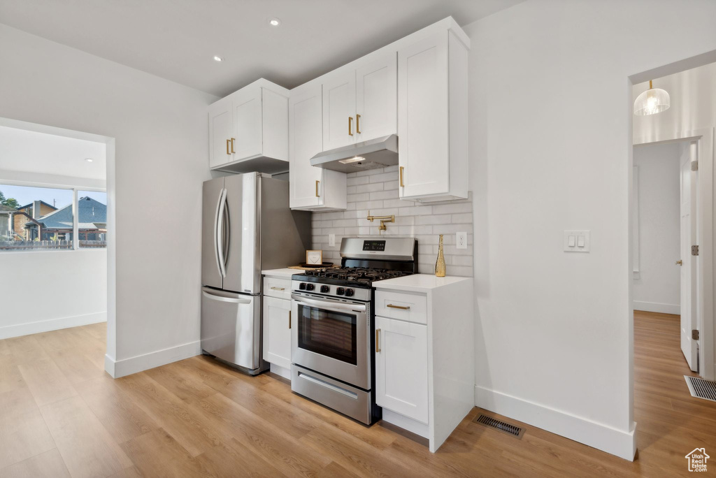 Kitchen with backsplash, white cabinetry, stainless steel appliances, and light wood-type flooring