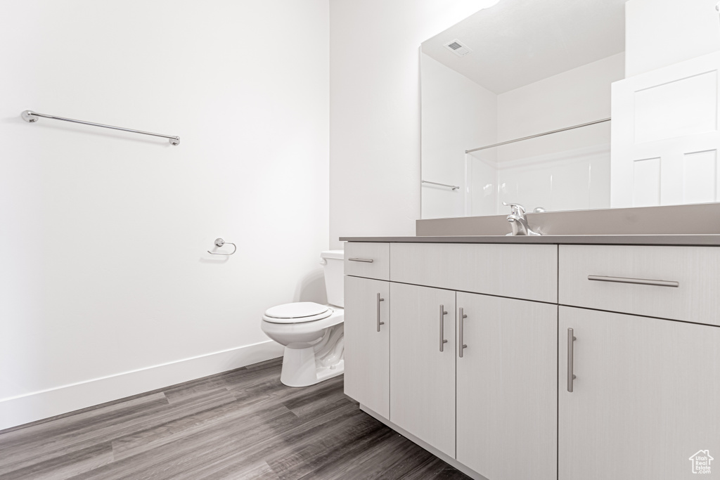 Bathroom with vanity, toilet, wood finished floors, baseboards, and a shower