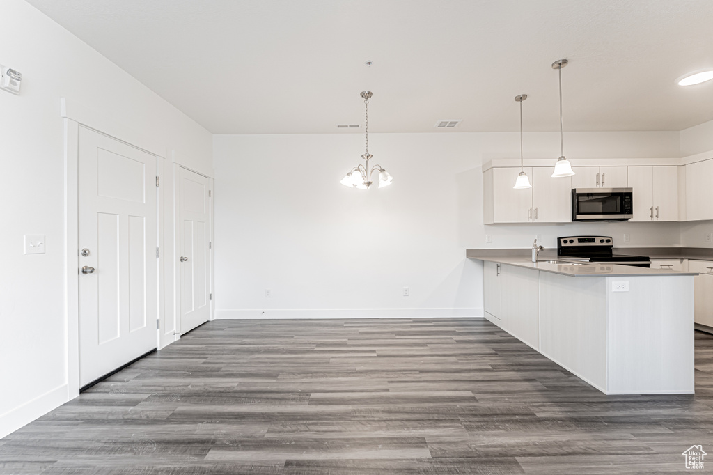 Kitchen with stainless steel microwave, electric range oven, a chandelier, baseboards, and wood finished floors