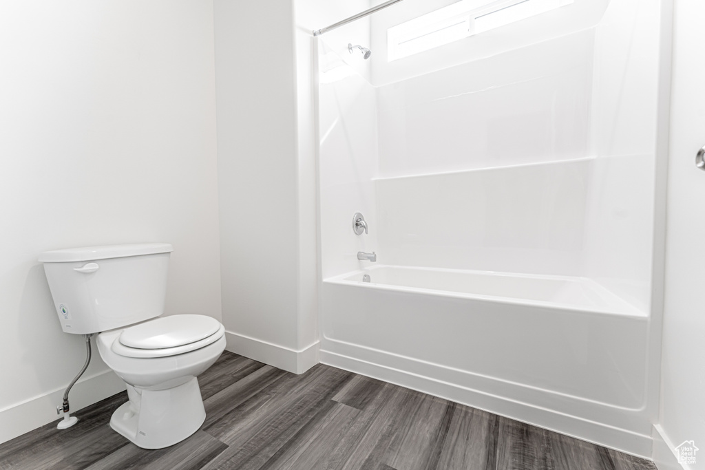 Bathroom featuring toilet, baseboards, bathing tub / shower combination, and wood finished floors
