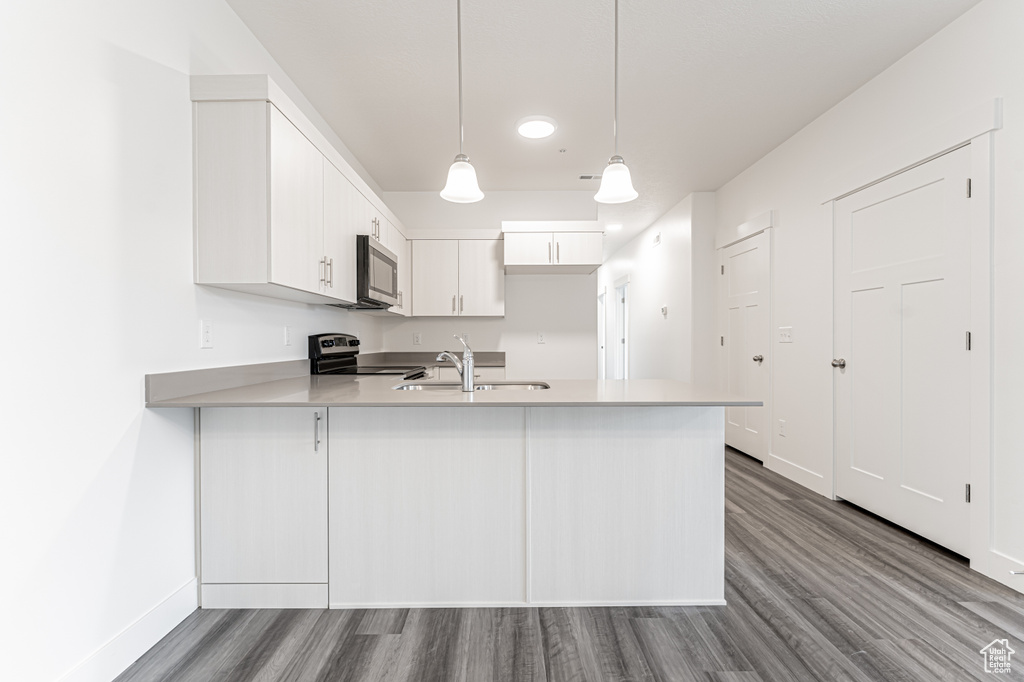 Kitchen featuring electric stove, a sink, a peninsula, dark wood finished floors, and light countertops
