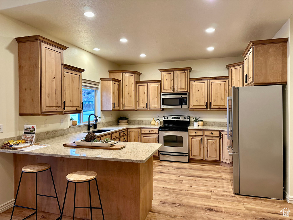 Kitchen featuring kitchen peninsula, a breakfast bar, stainless steel appliances, sink, and light hardwood / wood-style flooring