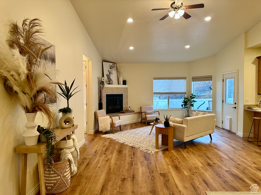 Living room featuring ceiling fan, vaulted ceiling, a tiled fireplace, and light hardwood / wood-style flooring