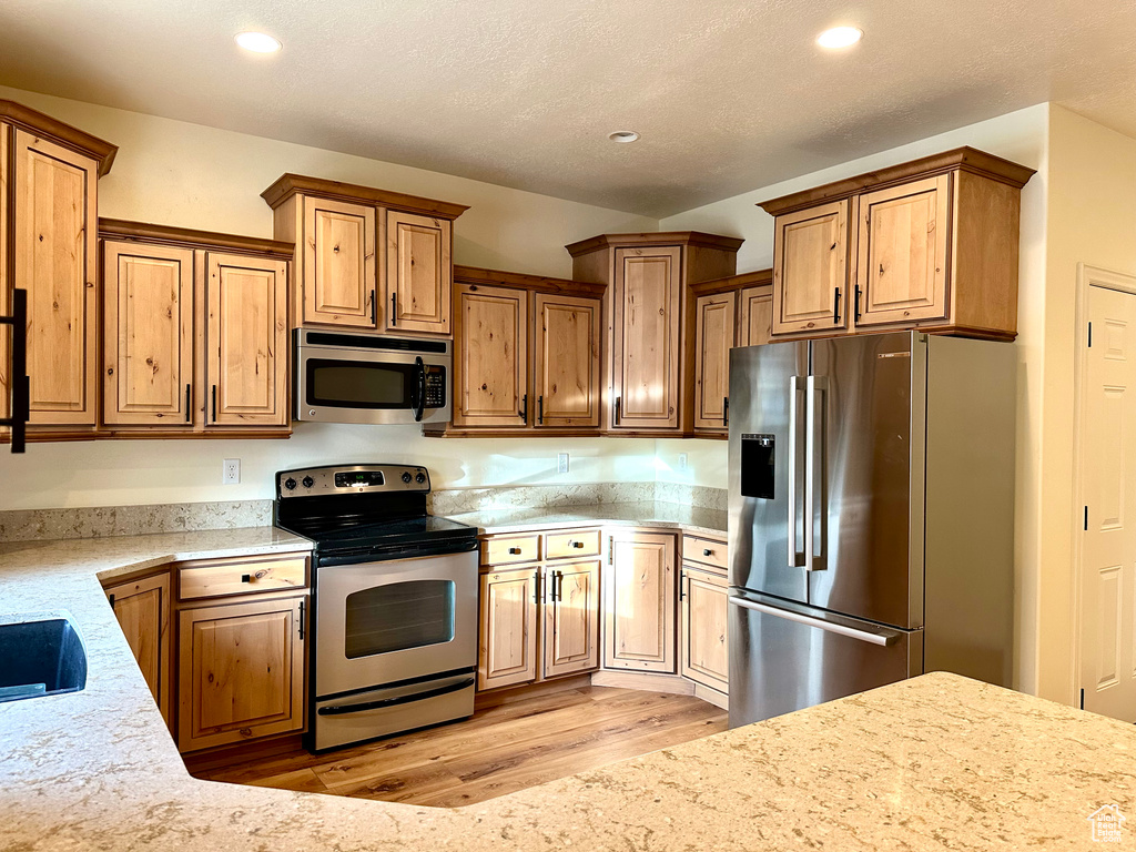 Kitchen with light stone counters, appliances with stainless steel finishes, a textured ceiling, and light wood-type flooring