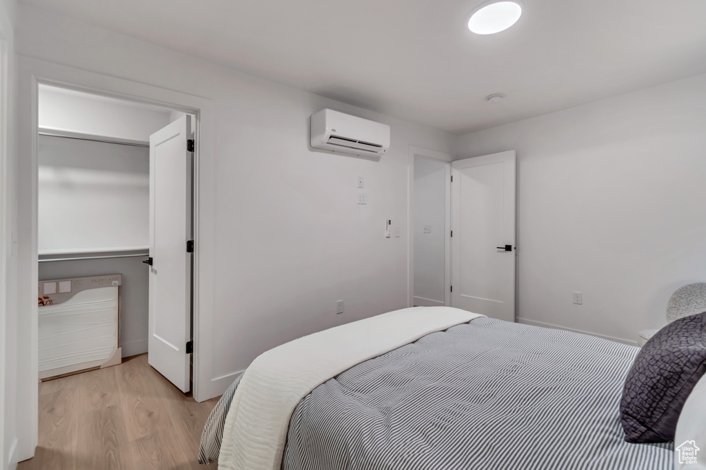 Bedroom with a wall mounted air conditioner and light hardwood / wood-style flooring