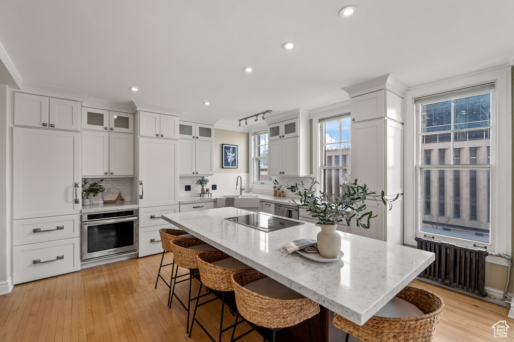 Kitchen featuring black electric cooktop, radiator, a kitchen island, oven, and white cabinets