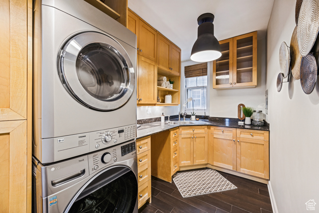 Laundry area with cabinets, stacked washer / drying machine, sink, and dark hardwood / wood-style flooring