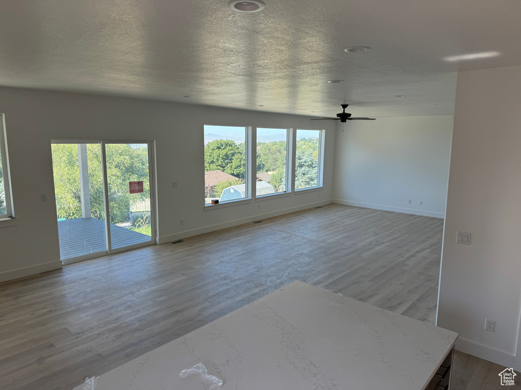 Unfurnished living room featuring a wealth of natural light, light hardwood / wood-style flooring, a textured ceiling, and ceiling fan