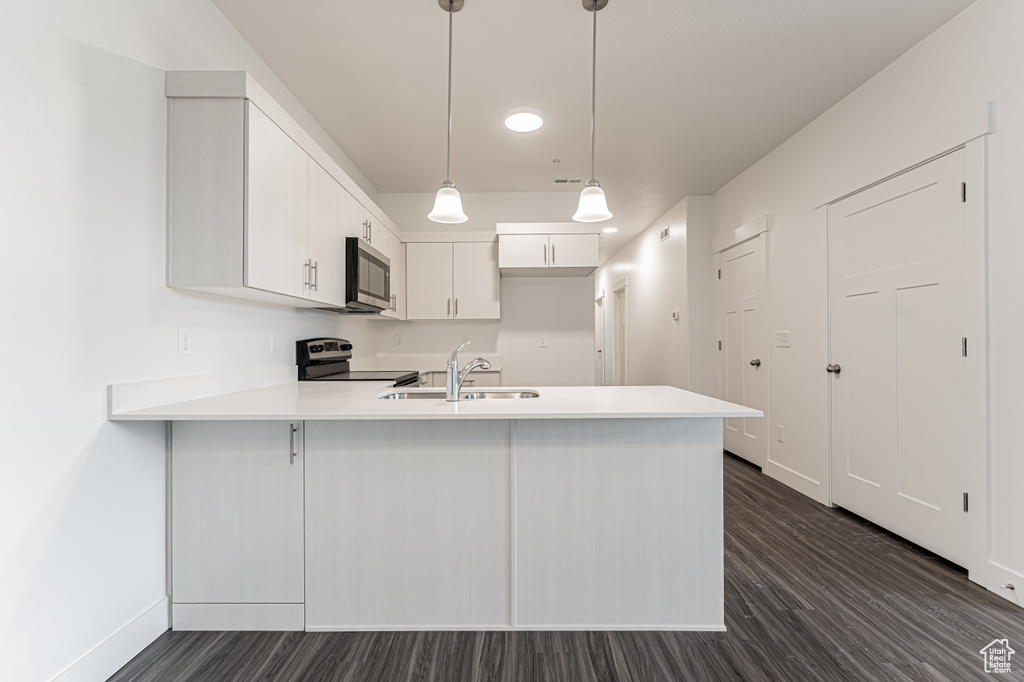 Kitchen featuring a sink, dark wood finished floors, stainless steel appliances, a peninsula, and light countertops