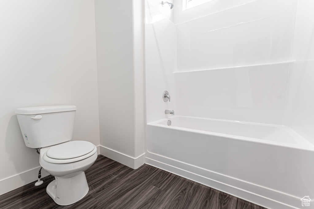Bathroom featuring toilet, shower / bathing tub combination, baseboards, and wood finished floors