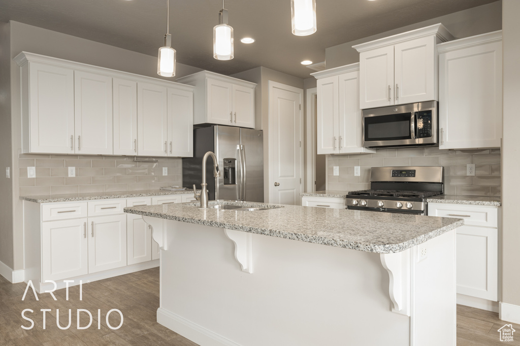 Kitchen featuring appliances with stainless steel finishes, white cabinets, hanging light fixtures, and a breakfast bar area