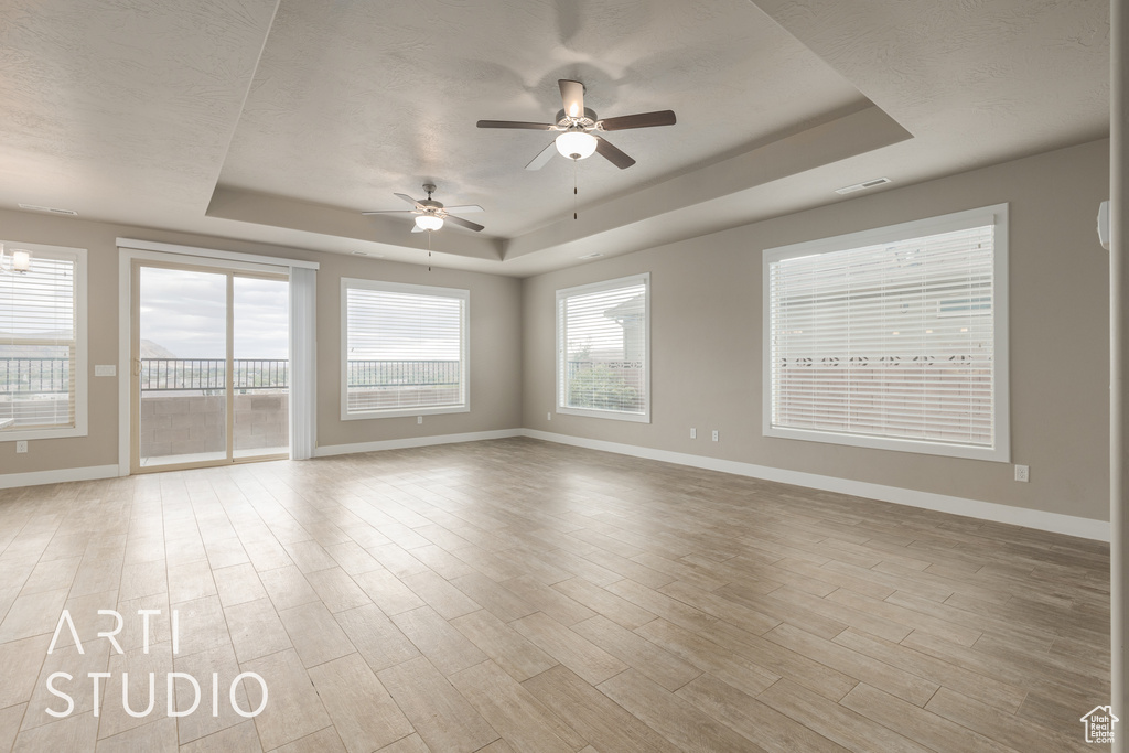 Spare room with a tray ceiling, plenty of natural light, and ceiling fan with notable chandelier