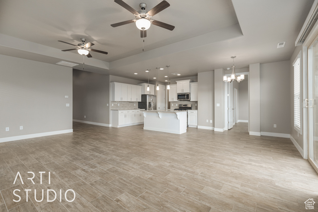 Unfurnished living room with a tray ceiling, light wood-type flooring, and ceiling fan with notable chandelier