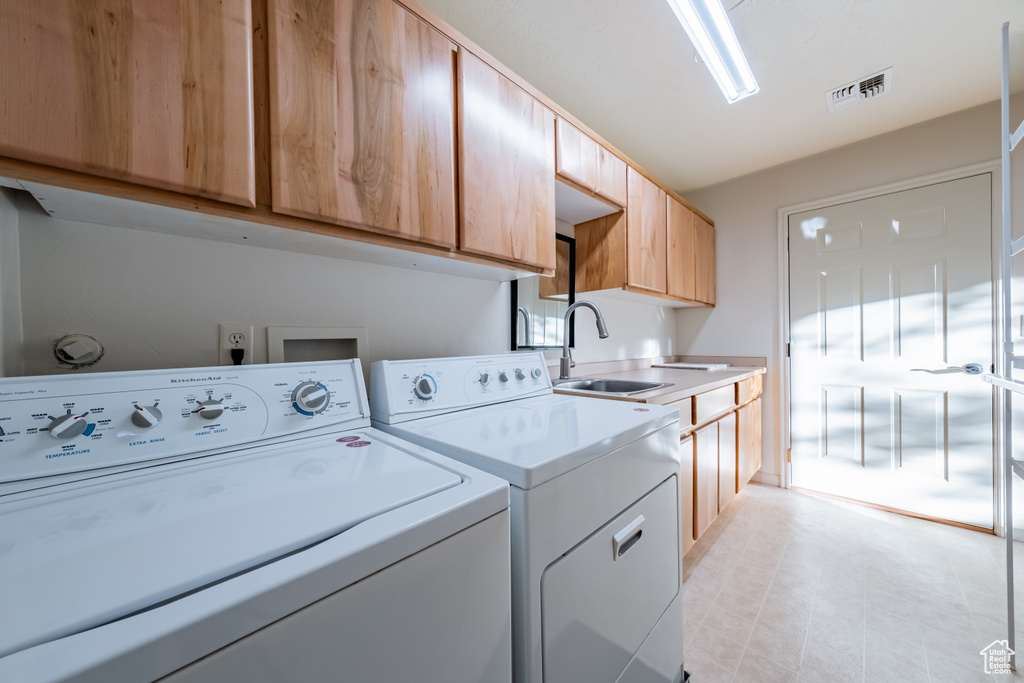 Clothes washing area with cabinets, sink, and washer and clothes dryer