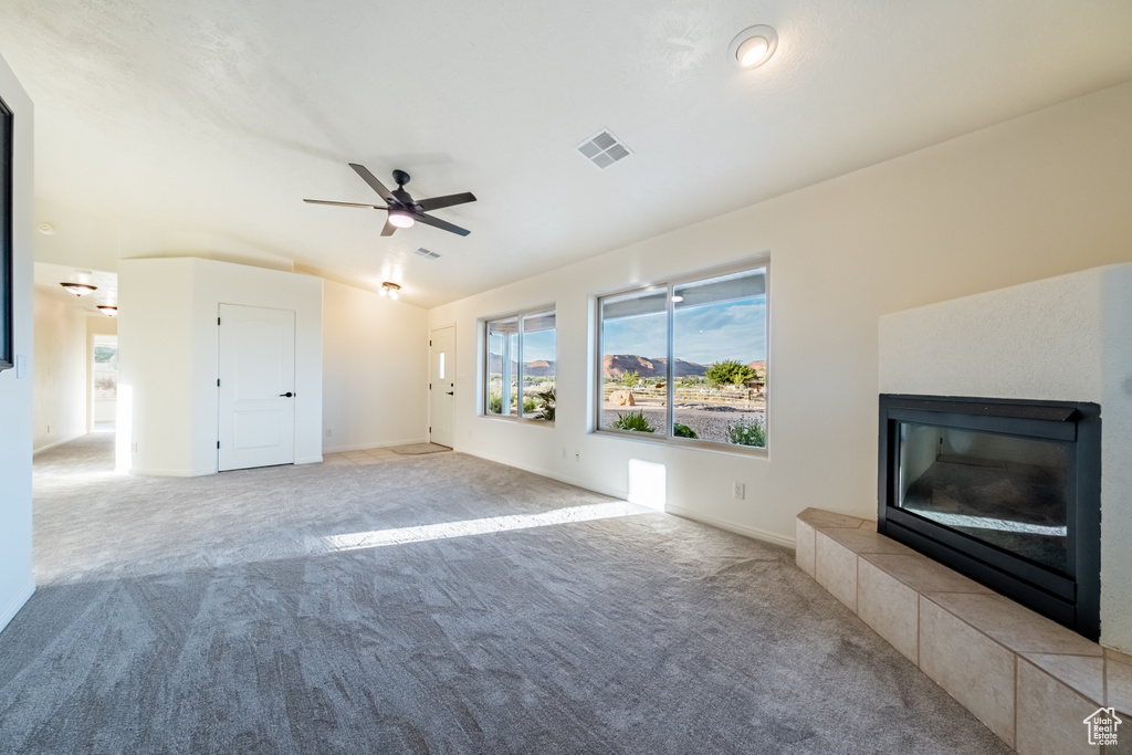 Unfurnished living room featuring ceiling fan, light colored carpet, and a tiled fireplace