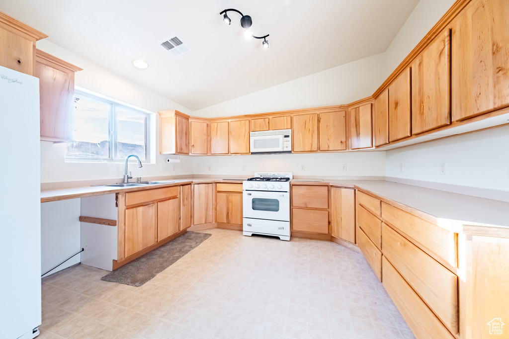 Kitchen featuring lofted ceiling, white appliances, sink, and light brown cabinets