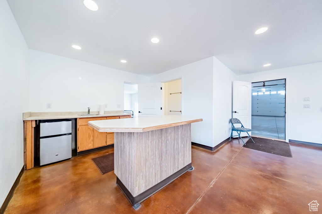 Kitchen with light brown cabinets, stainless steel refrigerator, sink, and a center island