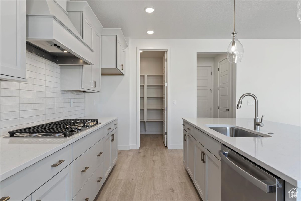 Kitchen with hanging light fixtures, premium range hood, white cabinetry, light hardwood / wood-style flooring, and stainless steel appliances