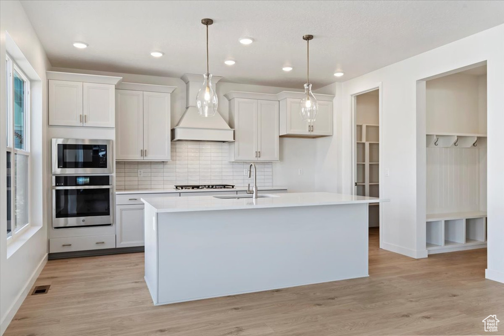 Kitchen with white cabinets, sink, a center island with sink, and pendant lighting