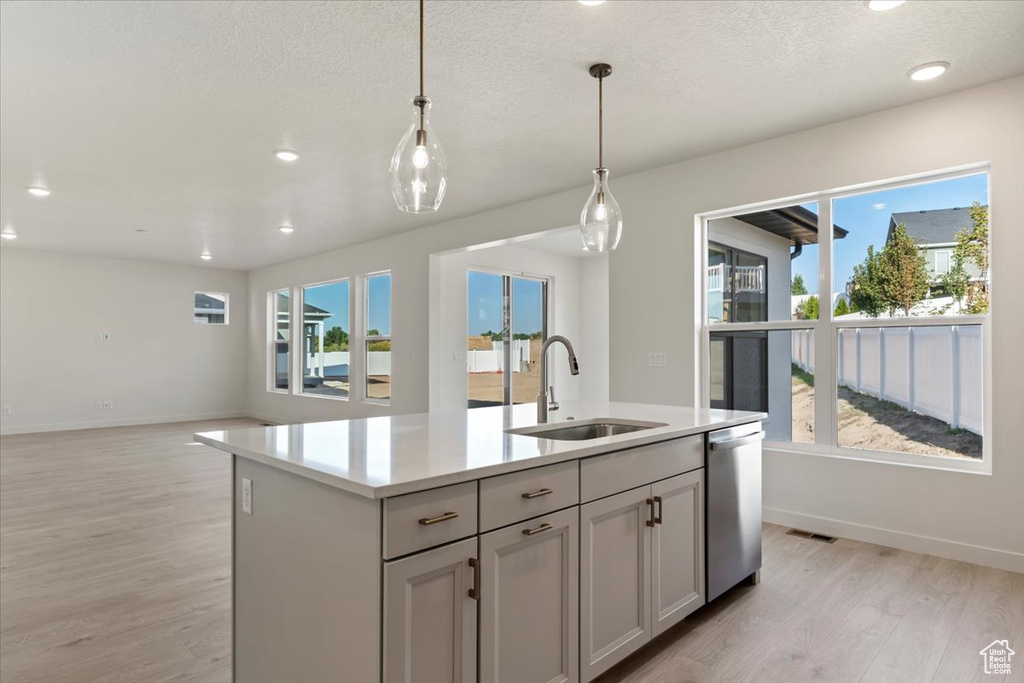 Kitchen with sink, a wealth of natural light, stainless steel dishwasher, and a center island with sink