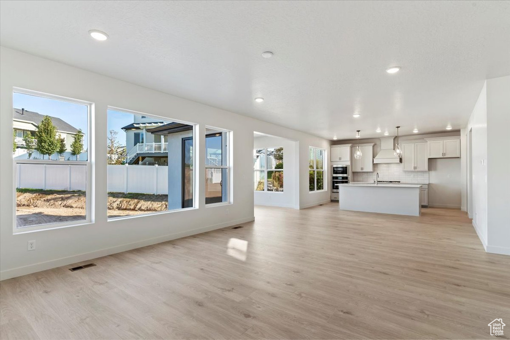 Unfurnished living room featuring sink, light hardwood / wood-style flooring, and plenty of natural light