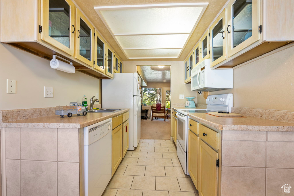 Kitchen with light brown cabinetry, sink, white appliances, and light tile patterned floors