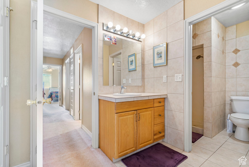 Bathroom featuring toilet, a textured ceiling, vanity, and tile walls