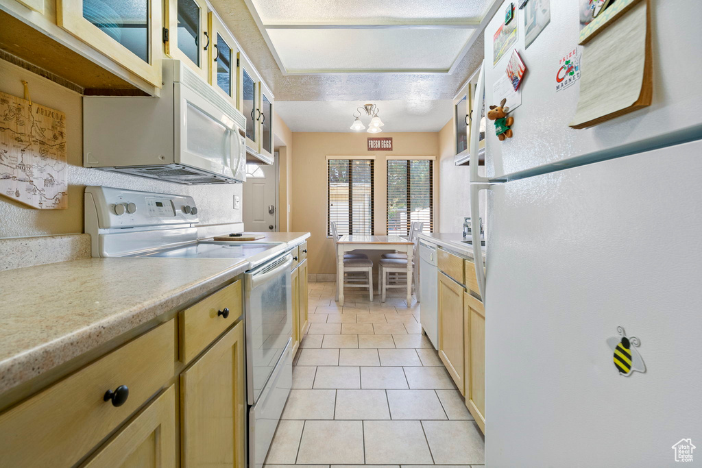 Kitchen with light brown cabinets, light tile patterned flooring, a notable chandelier, a textured ceiling, and white appliances