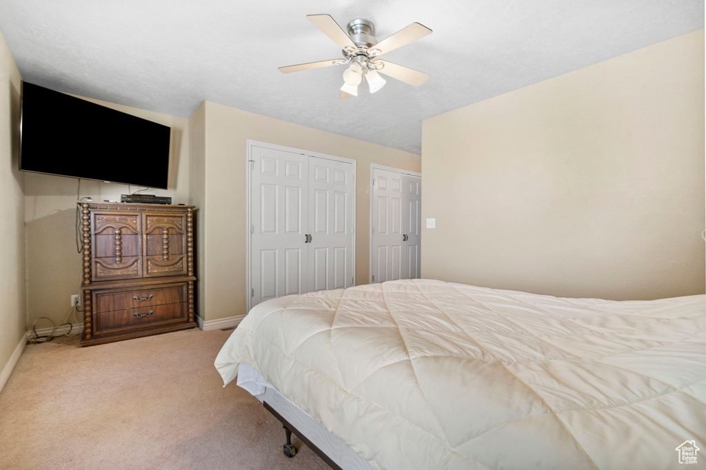 Carpeted bedroom with ceiling fan and two closets