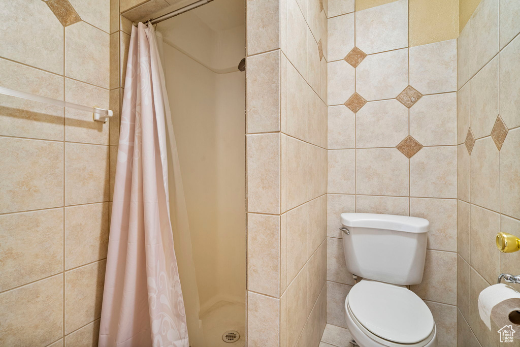 Bathroom featuring toilet, walk in shower, and tile walls