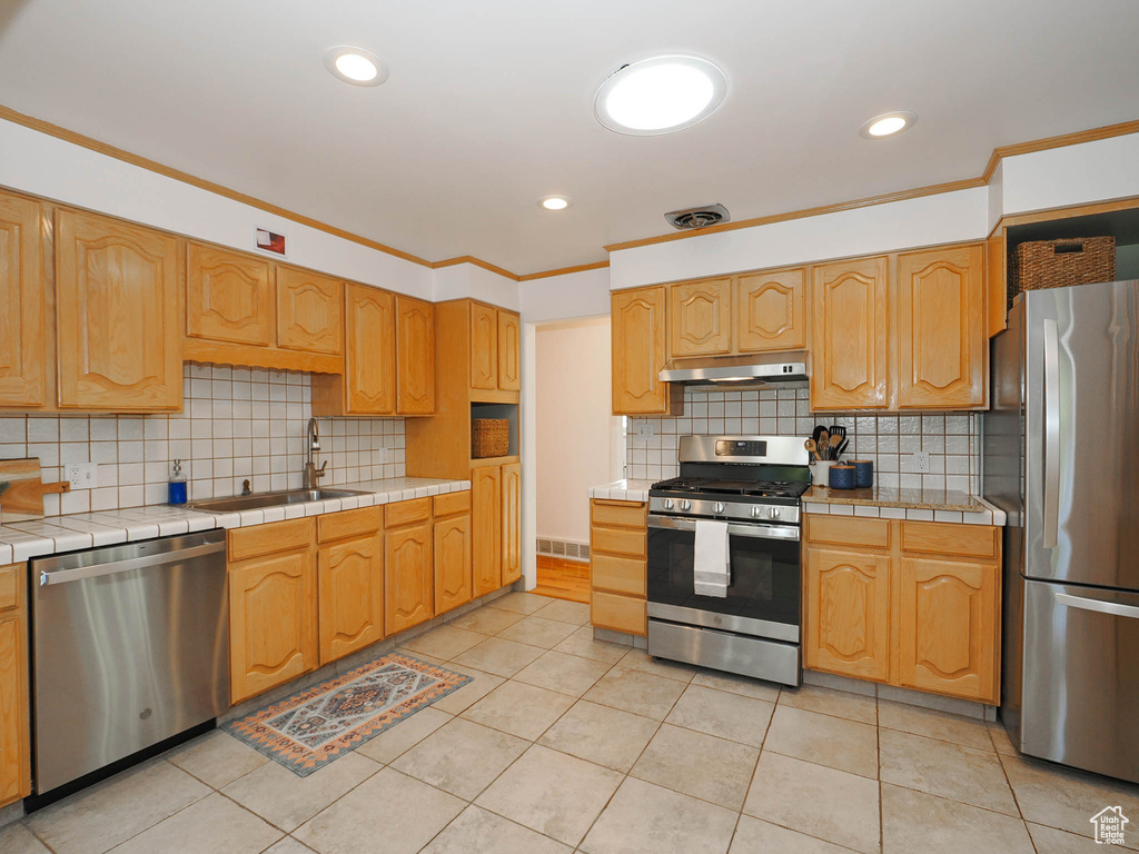 Kitchen with appliances with stainless steel finishes, tile counters, sink, and crown molding