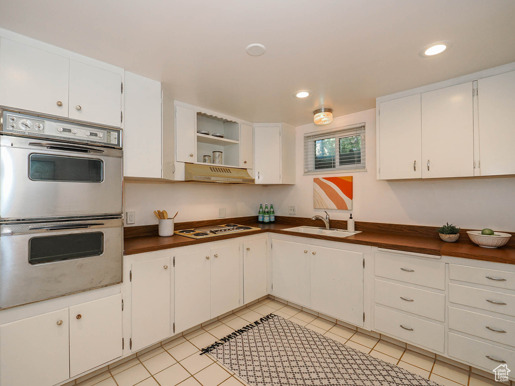 Kitchen featuring light tile patterned floors, white cabinetry, white gas cooktop, double oven, and sink