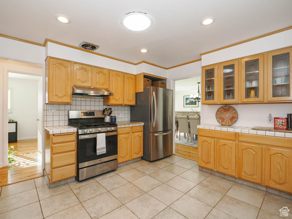 Kitchen with stainless steel appliances, ornamental molding, light tile patterned floors, and tile counters