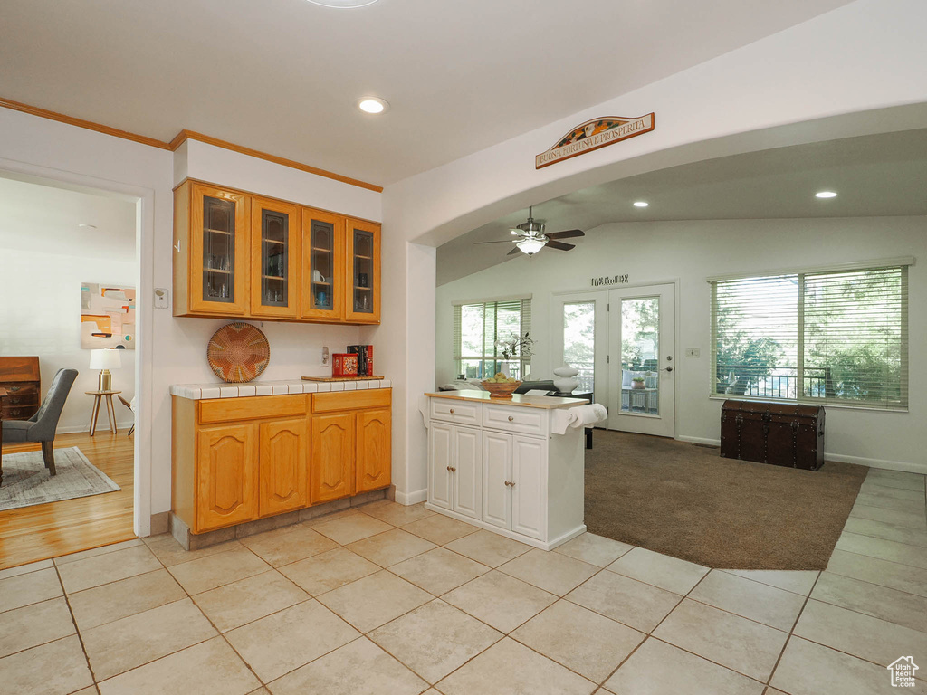 Kitchen with ceiling fan, lofted ceiling, light tile patterned floors, and tile countertops