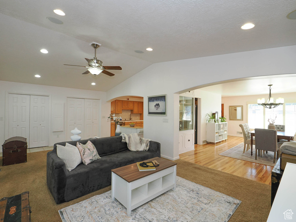 Living room featuring light hardwood / wood-style flooring, lofted ceiling, and ceiling fan with notable chandelier